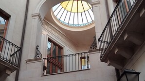 Ein mehrgeschossiges Atrium mit einer zentralen Kuppelkuppel, Balkonen mit schmiedeeisernen Geländern und einer Treppe zu einer oberen Etage.