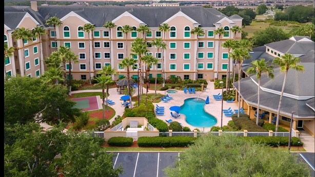 A hotel with a swimming pool, palm trees, and a view of the cityscape. - Suites at Lake Buena Vista close Disney Spring (Orlando)