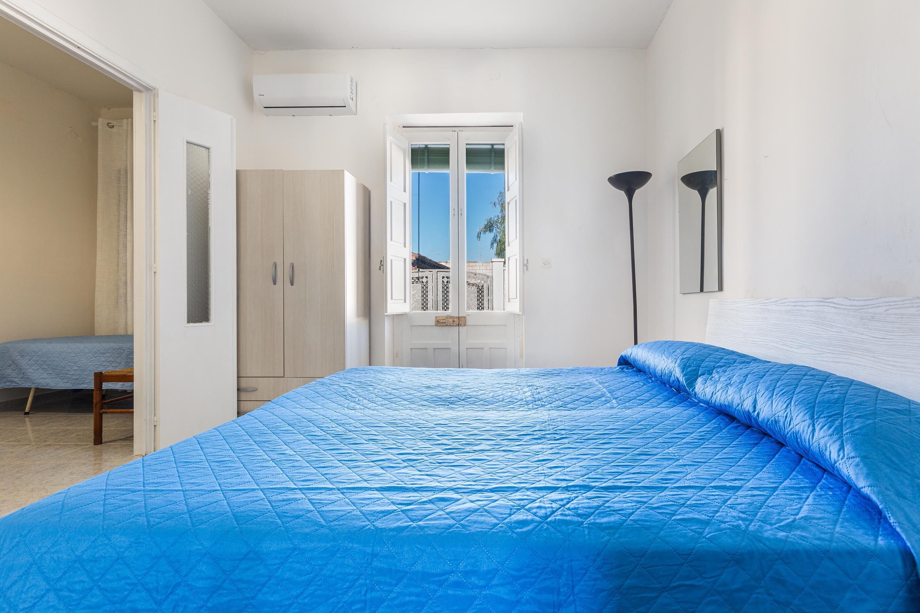 A bedroom with a large bed, a wardrobe, a window, and a door leading to another room.