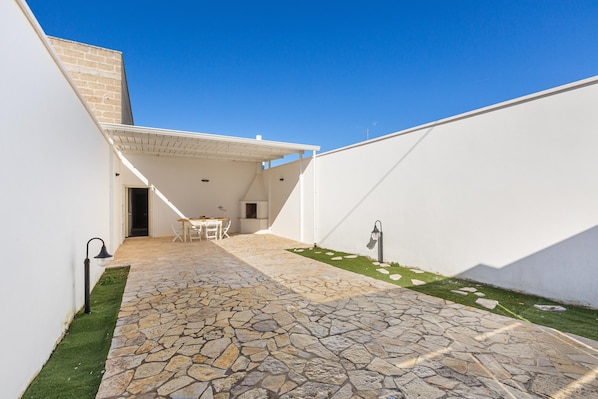 A stone-paved patio with a white wall and a small grassy area.