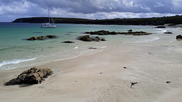 A beach with clear water, a sailboat, and rocky outcrops. - Fishermans Holding (Isle of Lewis)