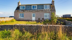 A two-story house with a stone facade, a front door, and a small porch with chairs. - Fishermans Holding (Isle of Lewis)