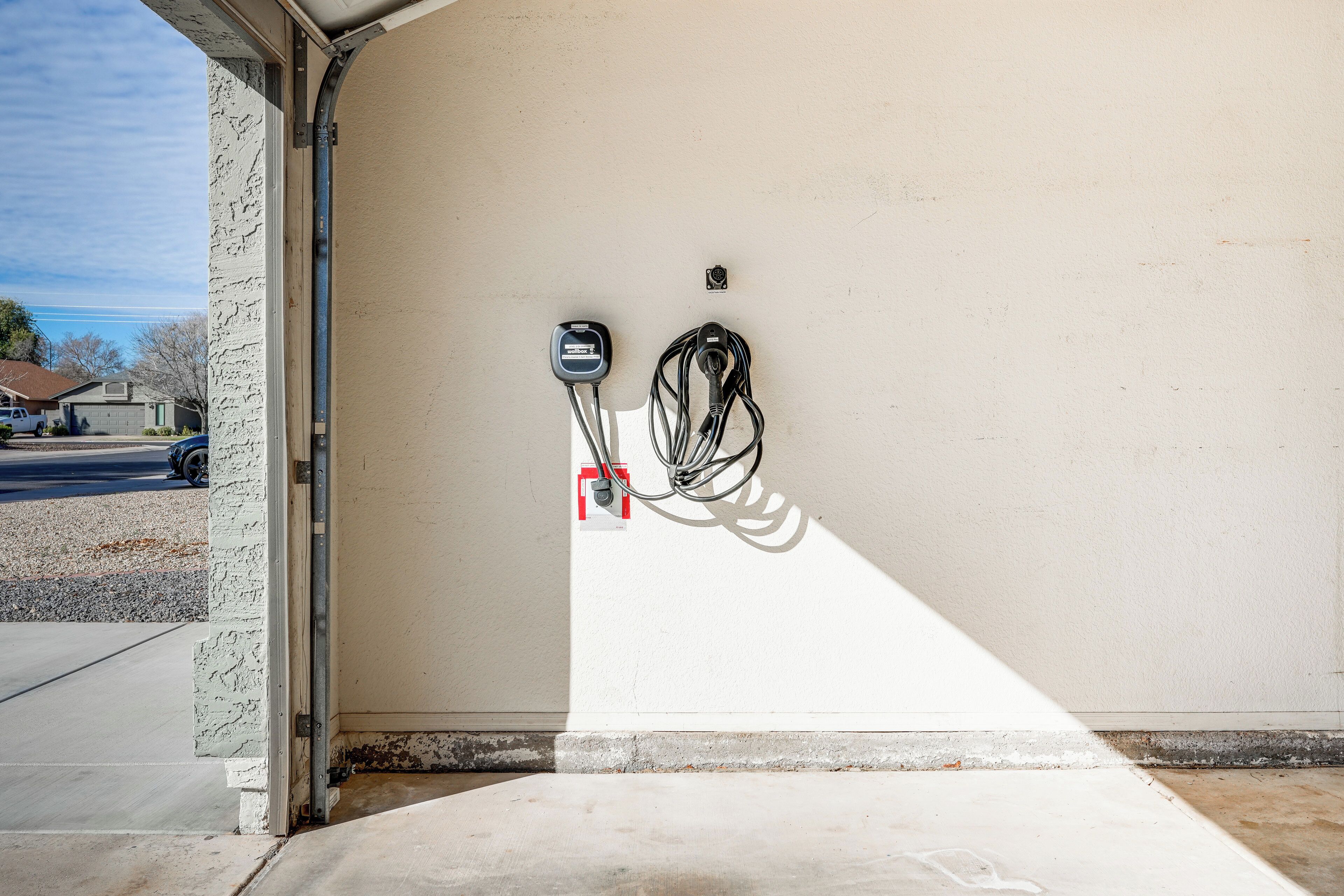 En garage med betongulv og hvide vægge. Der er en stikkontakt og et kabel hænger på væggen.