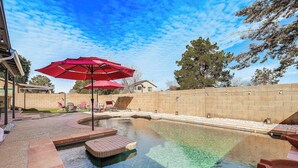 A swimming pool with red umbrellas, a brick deck, and a stone wall.