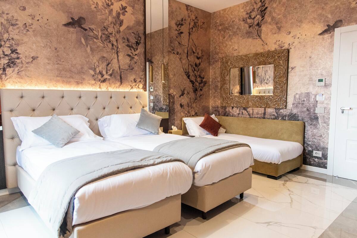 A hotel room with two beds, a large mirror, and a wall with a floral mural.