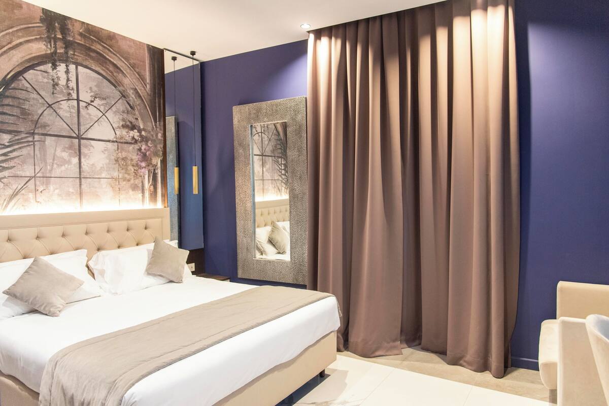 A modern bedroom with a large bed, a headboard with a window, a mirror, and a view of the outdoors.