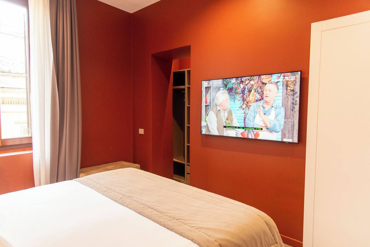 A hotel room with a bed, a television mounted on the wall, and a window with curtains.