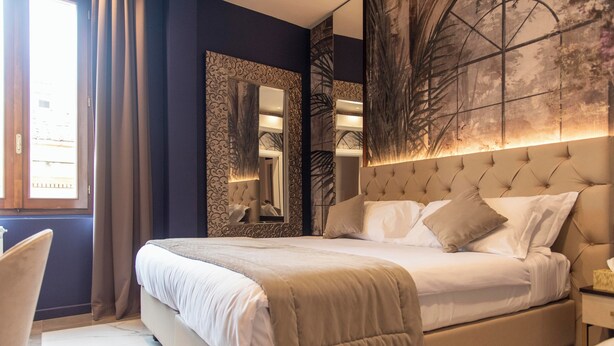 A bedroom with a large bed, a nightstand, a chair, and a large mirror. - Adelaide Suite Dreams (Rome)
