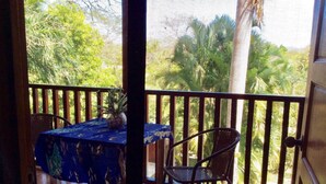 A balcony with a table and chairs, a potted plant, and a view of greenery. - TREE HOUSE PLAYA SAMARA (Playa Samara Guanacaste Province)