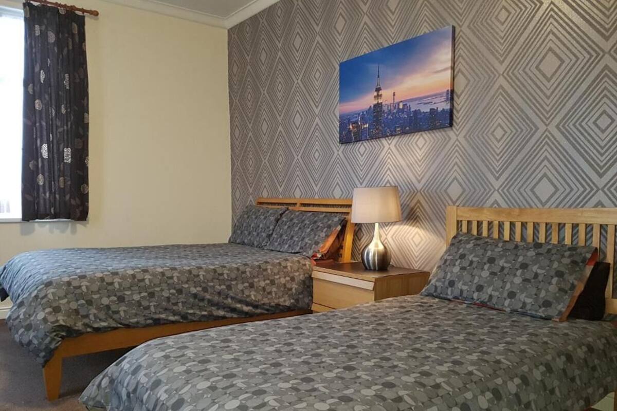 A bedroom with two beds, a nightstand, a lamp, and a cityscape painting on the wall.