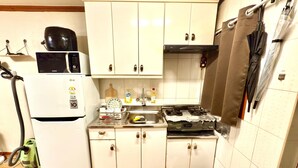 Pieni, käytännöllinen keittiö, jossa on valkoiset kaapit, mikroaaltouuni, jääkaappi, pesuallas ja liesi.