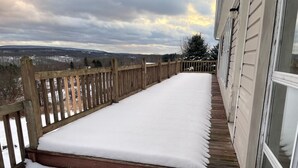 Une terrasse en bois recouverte de neige, une vue sur un paysage enneigé et un bâtiment avec une fenêtre.
