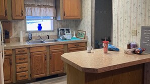 Une cuisine avec des meubles en bois, un plan de travail en granit, une fenêtre ornée d’un vase bleu et une pancarte de bienvenue.