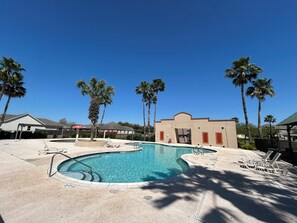 A swimming pool with lounge chairs, palm trees, and a building with a red door.