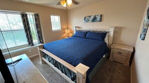 A bedroom with a bed, nightstands, a lamp, a painting, and a window with blinds.