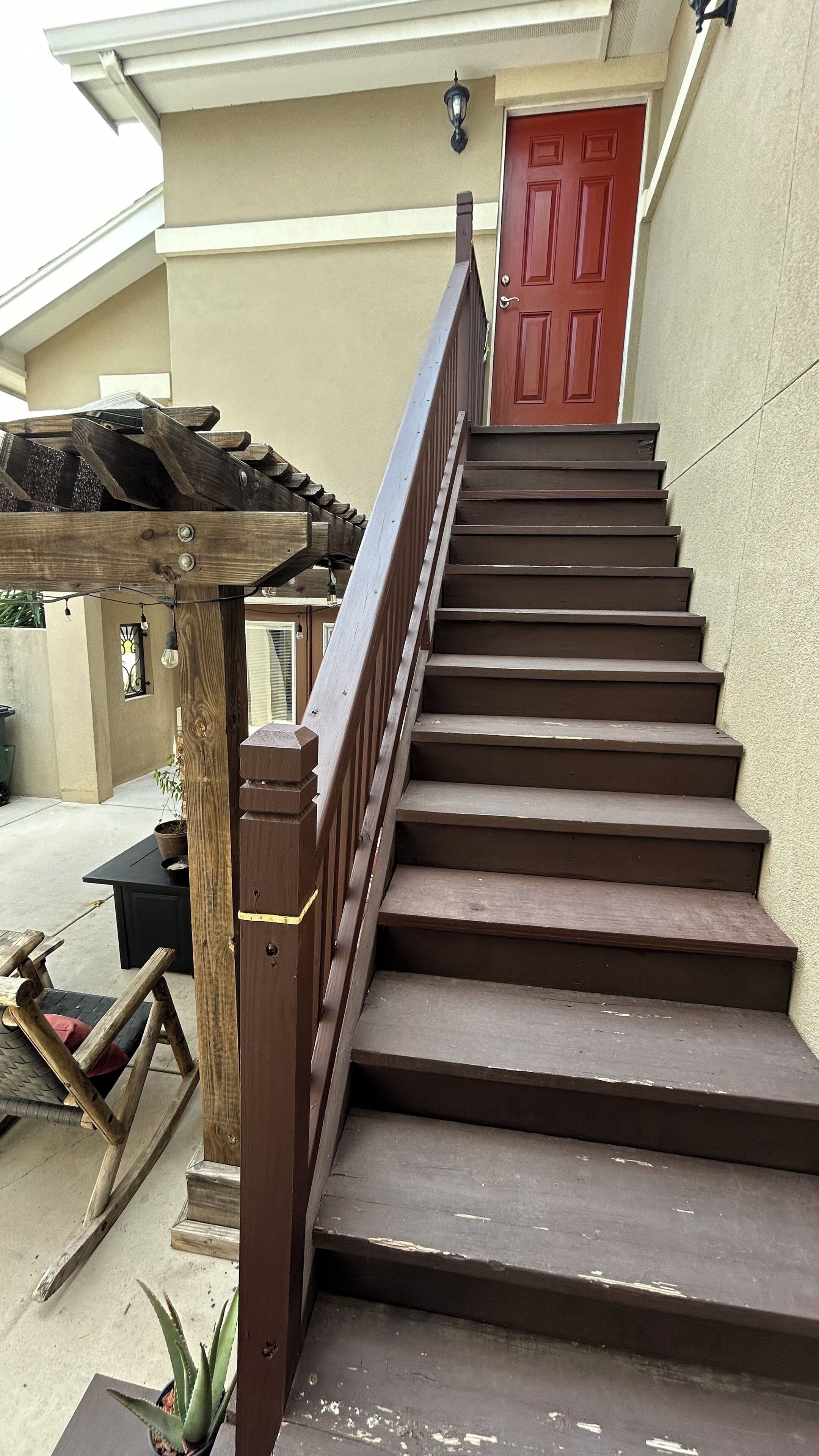 Una escalera de madera con barandilla de metal que lleva a una puerta roja.