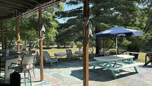 An outdoor patio area with picnic tables, chairs, and a grill.