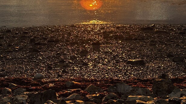 A sunset over a rocky beach with calm water reflecting the sky.