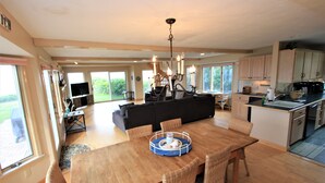 A spacious living area with a wooden dining table, wicker chairs, a black sofa, and a chandelier. - 8 The Gridiron (Sandwich)