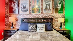 Un dormitorio con pared de ladrillo, una cama con dos almohadas y carteles en la pared.