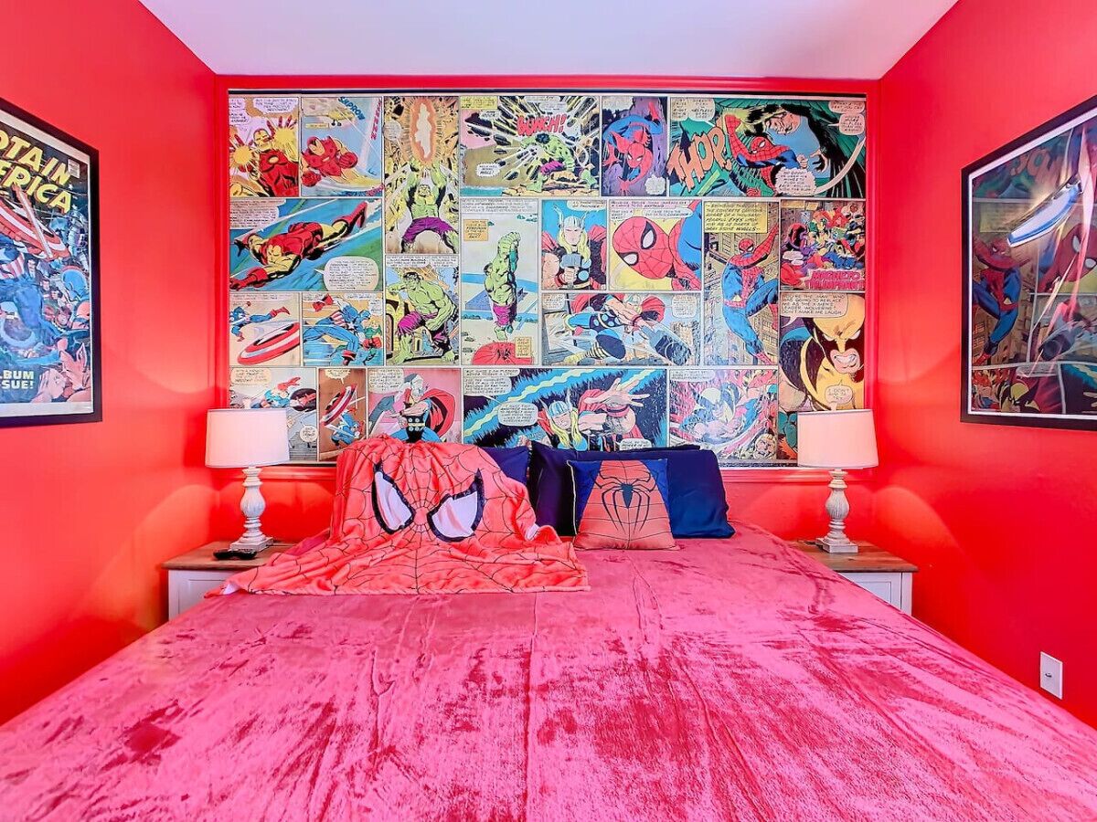 A bedroom with a vibrant red color scheme, featuring a large Spider-Man themed bedspread and multiple comic book posters on the walls.