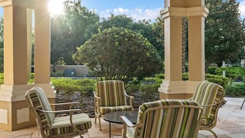 Un espace extérieur aménagé avec des sièges, protégé par un toit, comprenant des chaises à rayures et une petite table, le tout entouré de verdure et d’arbres.
