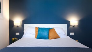 A neatly made bed with white linens and two decorative pillows, a white headboard, and wall-mounted lights on either side. - Terrasse Manuela Apartment 1 (Napoli)