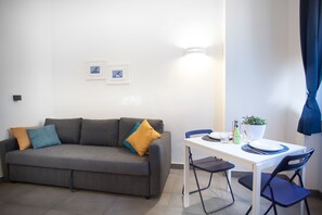 Un salon moderne avec un canapé gris, des coussins bleus et jaunes, une table à manger blanche avec des chaises bleues et une plante en pot.