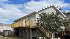 Une maison à deux étages avec une terrasse en bois et un arbre devant.
