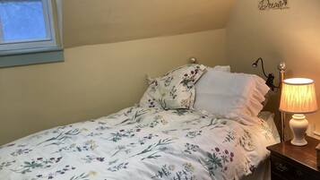 A bedroom with a single bed, a bedside lamp, a small wooden nightstand, and a window with a view of trees.