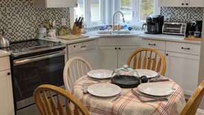 A modern kitchen with white cabinets, a black stove, and a dining table set for four. - Rustic and private farmhouse close to Lackawanna State Park, near Elk Mtn Ski  (Dalton)