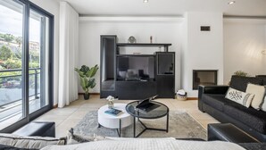 A modern living room with a large window, a fireplace, a black sofa, a coffee table, and a TV. - Til Home by Homie in Funchal (Funchal)