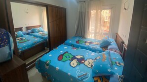 A bedroom with two beds, each covered with blue bedding featuring cartoon characters. There is a large mirror on one wall and a window with curtains. - Luxurious Modern Apartment (Madinaty)