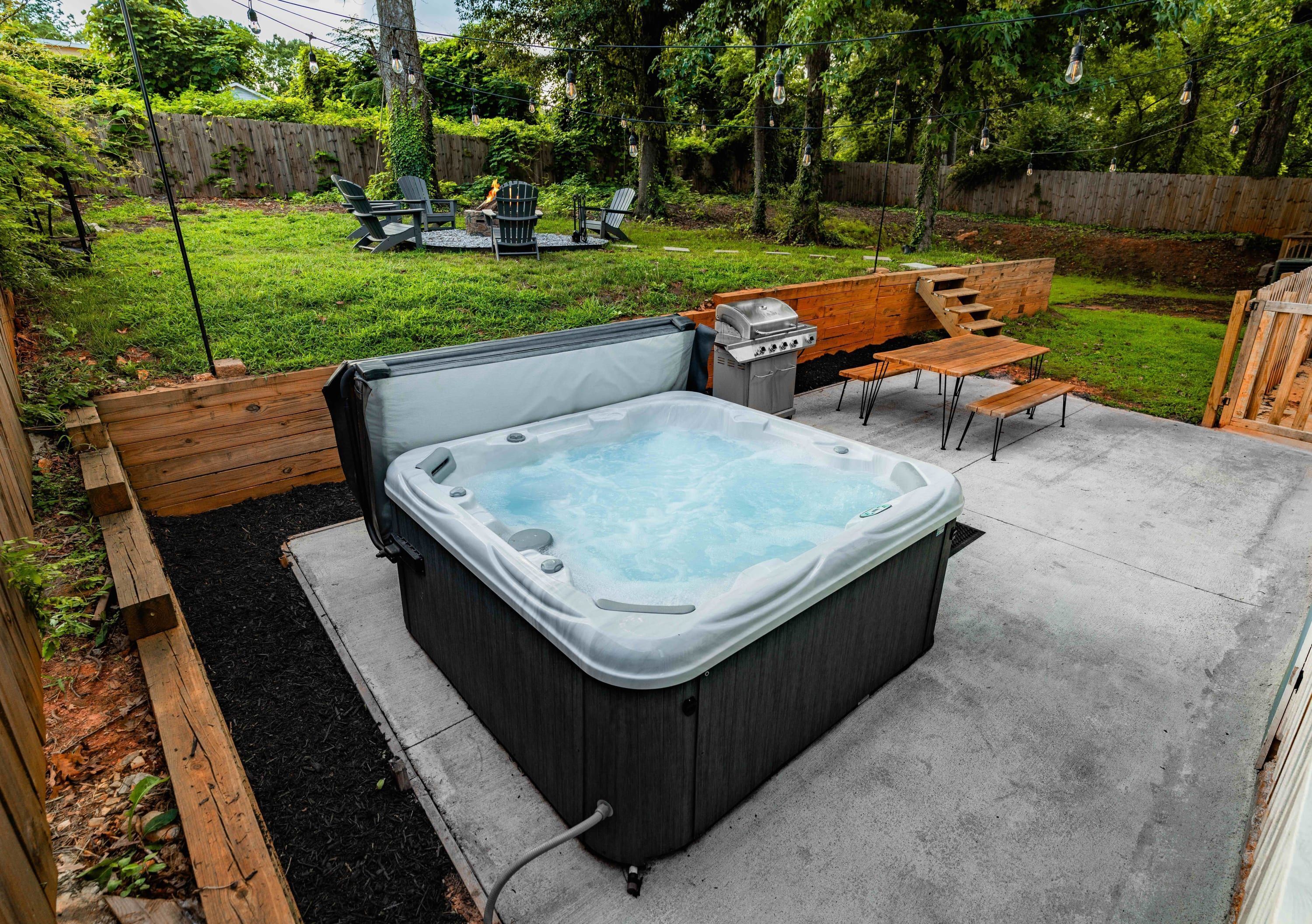 A hot tub in a backyard with a wooden deck, a grill, and outdoor seating.