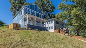 Stunning two-story home with a front porch and staircase, set amidst a lush hillside and mature trees.