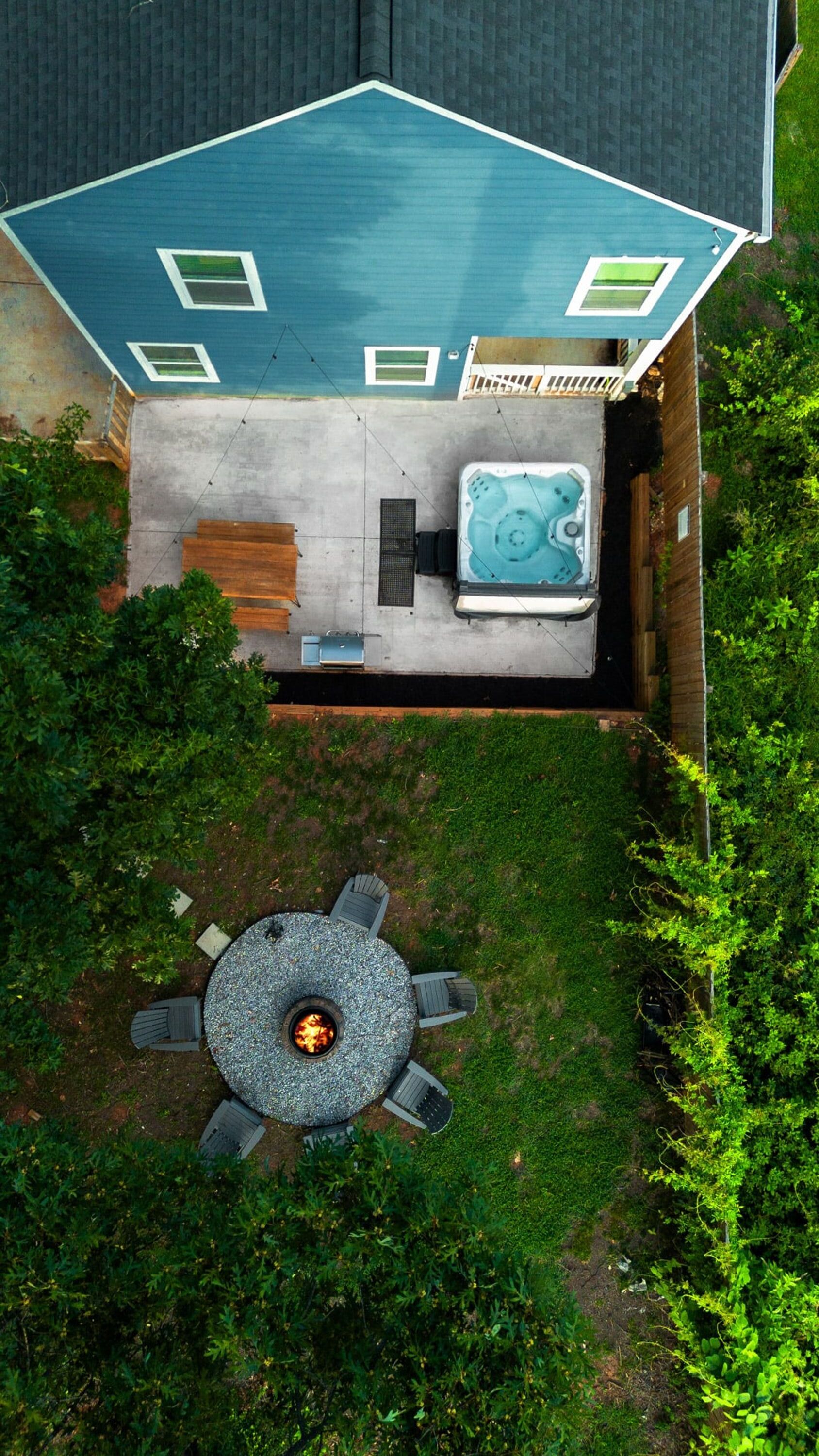 An aerial view of a backyard with a hot tub, a fire pit, and a patio table with chairs.
