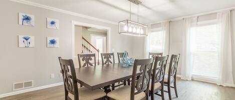 A dining room with a wooden table and chairs, a chandelier, and artwork on the walls.