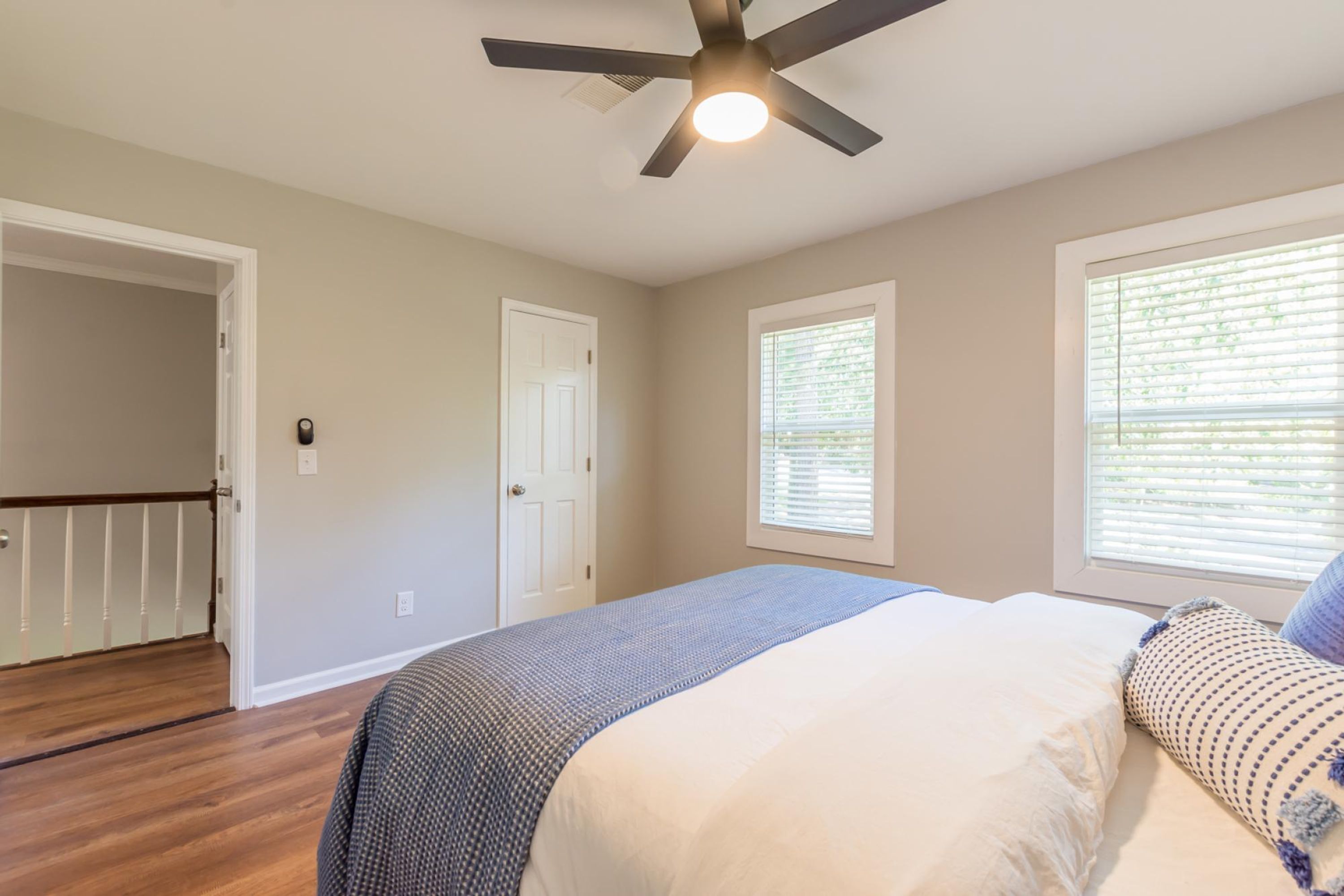 A bedroom with a bed, a ceiling fan, a window with blinds, and a door.