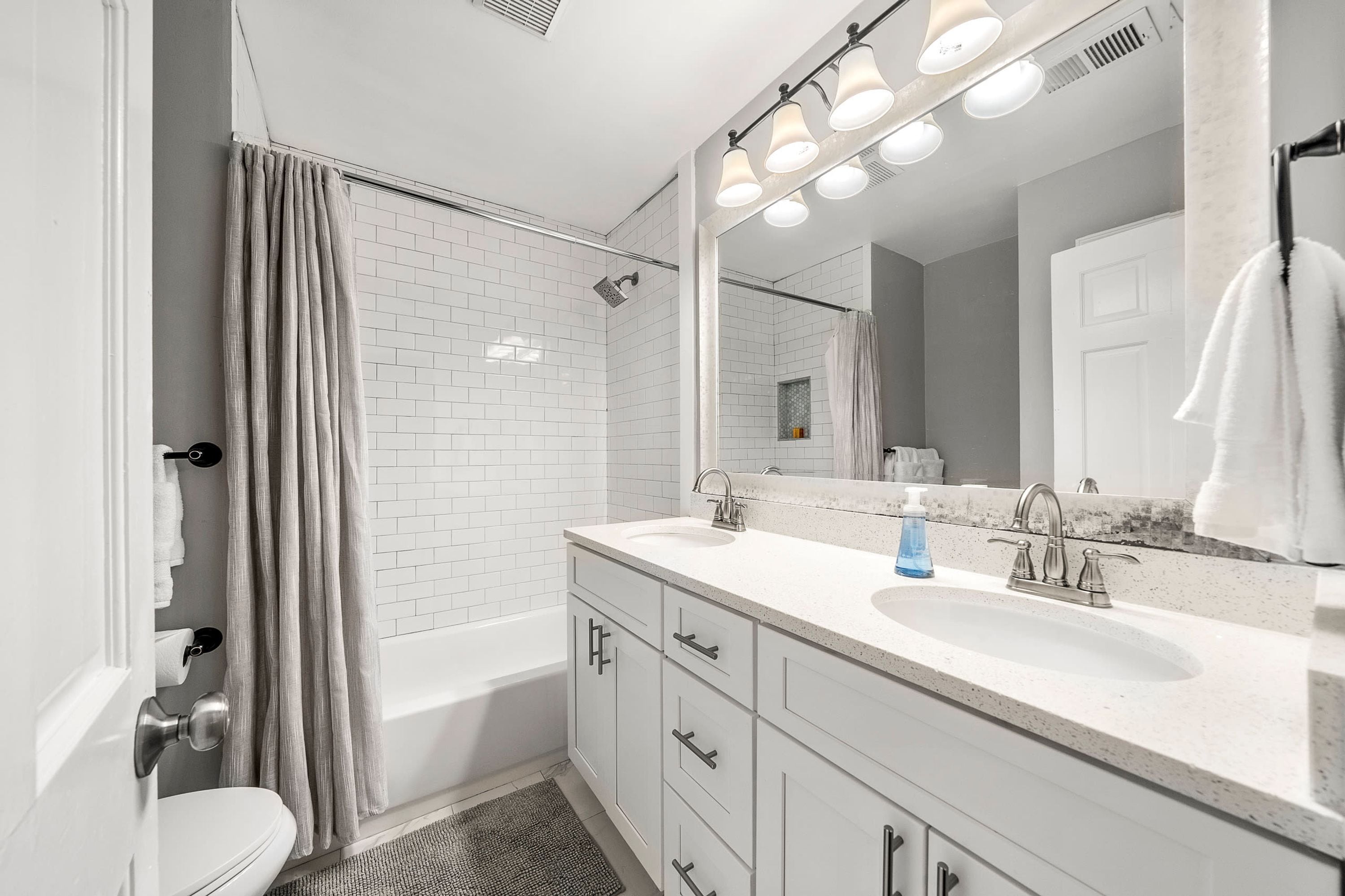 Een moderne badkamer met een wit toilet, een douche met gordijn, een grote spiegel en een wastafel met aanrecht.
