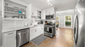 Une cuisine moderne avec des meubles blancs, des appareils en acier inoxydable et une vue sur l’extérieur.