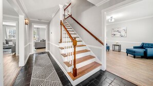 Un intérieur moderne avec un escalier, un salon doté de canapés bleus et un couloir menant à une autre pièce.