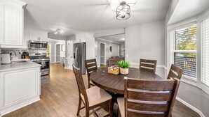 Une cuisine moderne avec des meubles blancs, un îlot central et un coin repas comprenant une table et des chaises en bois.