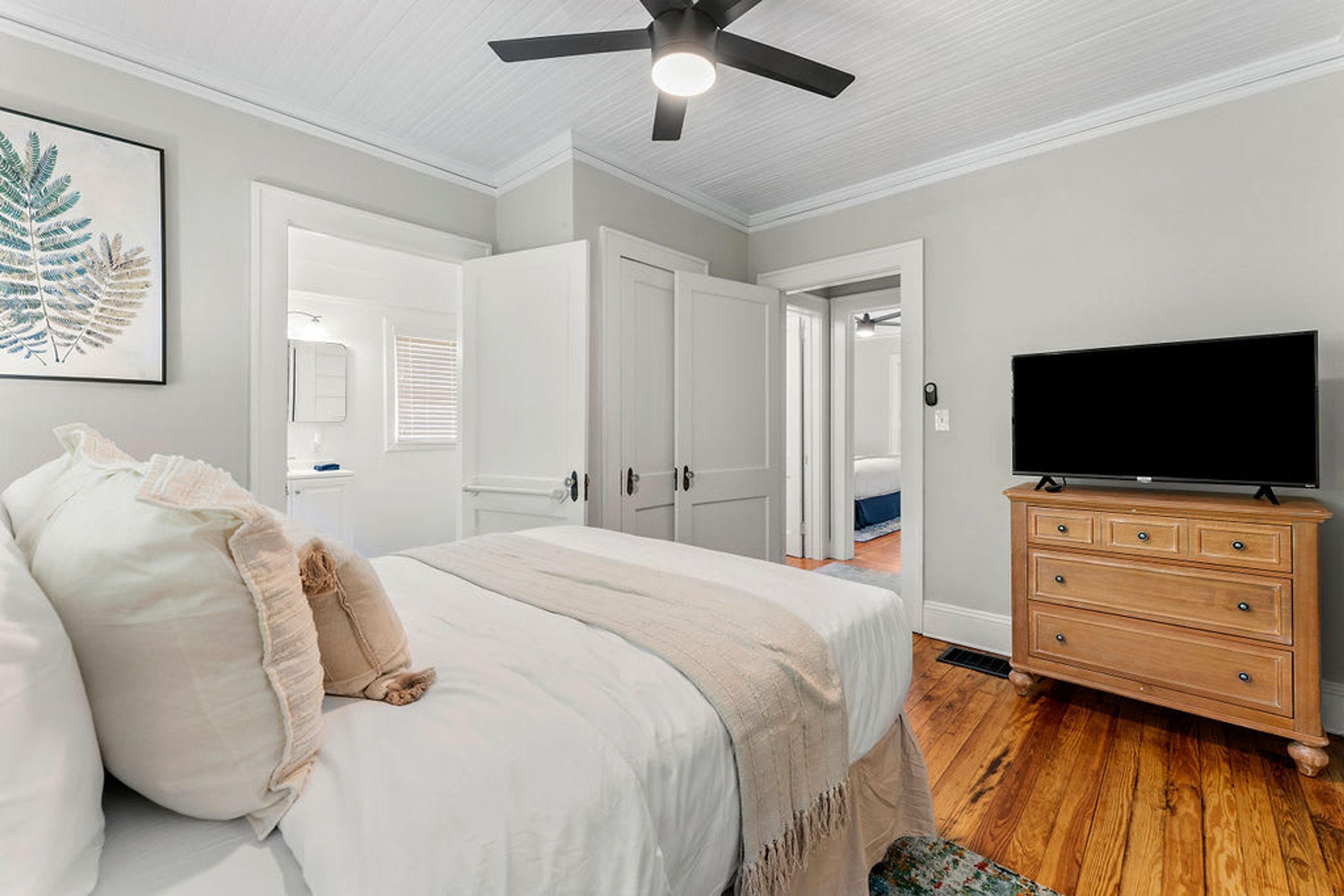 Une chambre à coucher comprenant un lit, une commode, un téléviseur et un ventilateur de plafond.