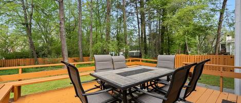 An outdoor deck with a table and chairs, surrounded by a wooden fence and trees.
