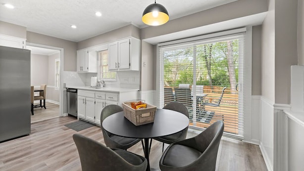 A modern kitchen with white cabinets, a dining area with a round table and chairs, and a large window with blinds. - Beautiful Newly-renovated Home in Indian Hills (Marietta)
