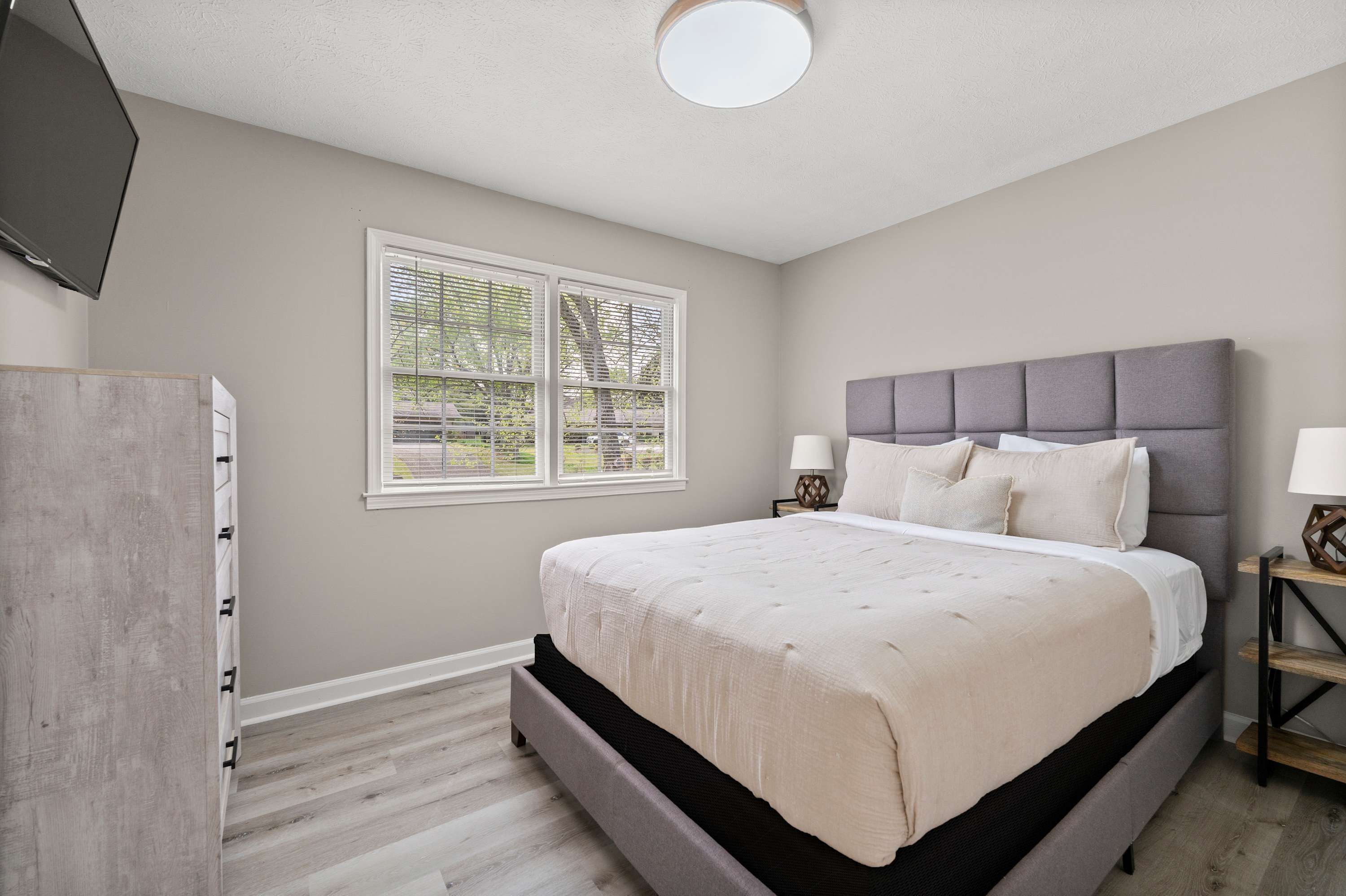A bedroom with a bed, bedside tables, a TV, and a window with blinds.