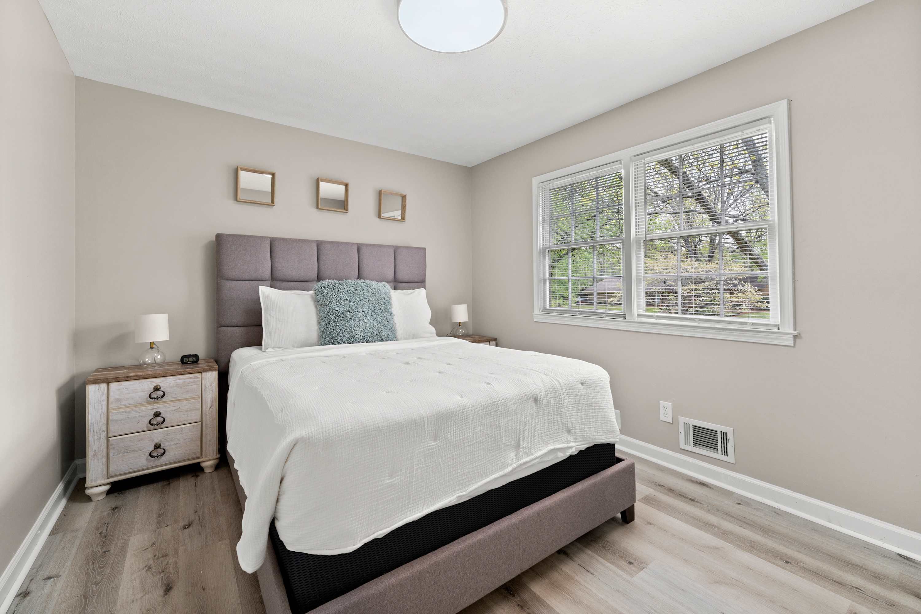 A bedroom with a bed, nightstands, a window with blinds, and a ceiling light.