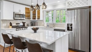 A modern kitchen with white cabinetry, a stainless steel refrigerator, a large island with bar stools, and pendant lighting. - Beautiful and Quiet Newly Renovated 4 Bedroom Retreat (Atlanta)
