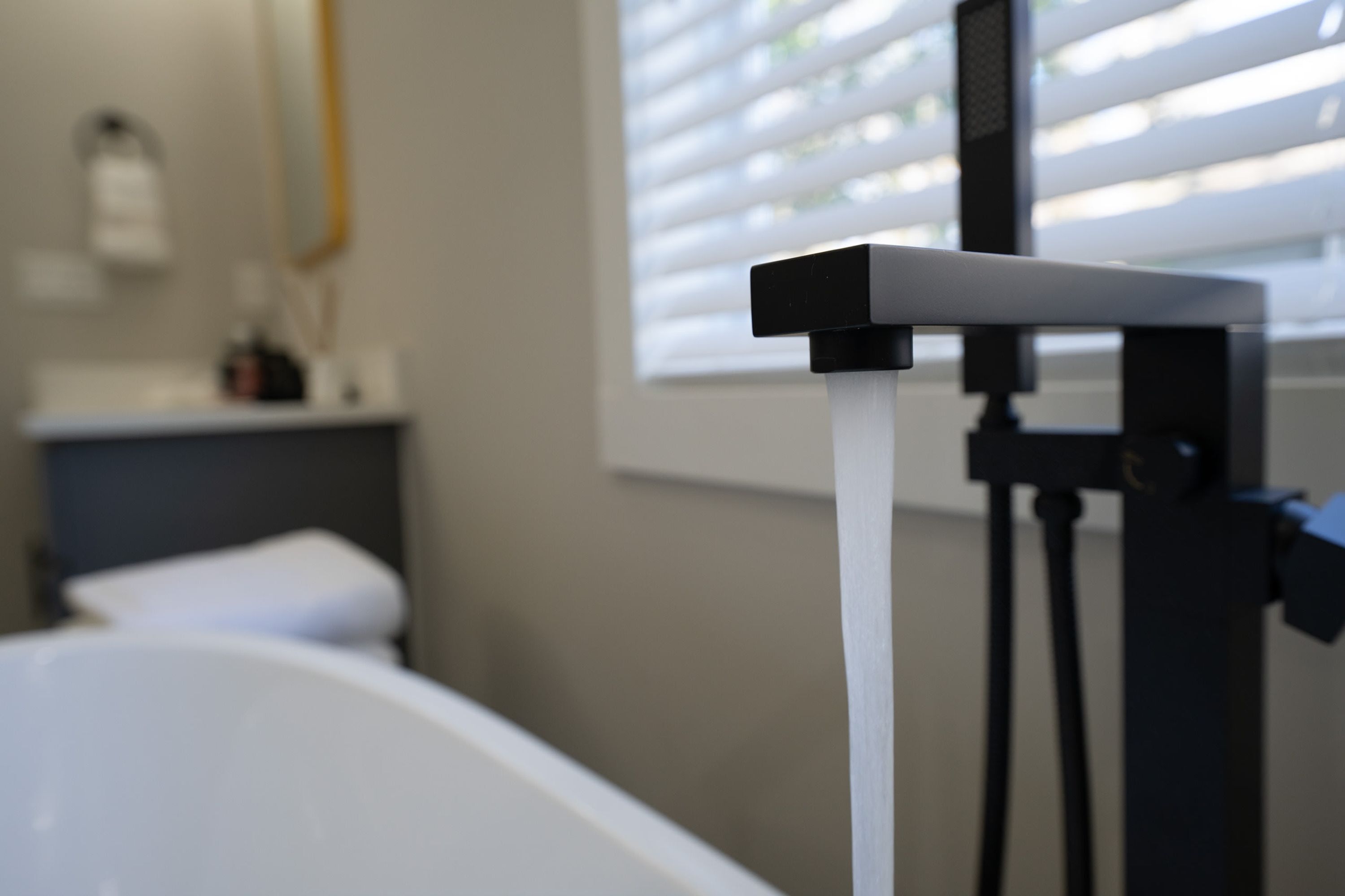 A bathroom with a white bathtub, a faucet, and a window with blinds.