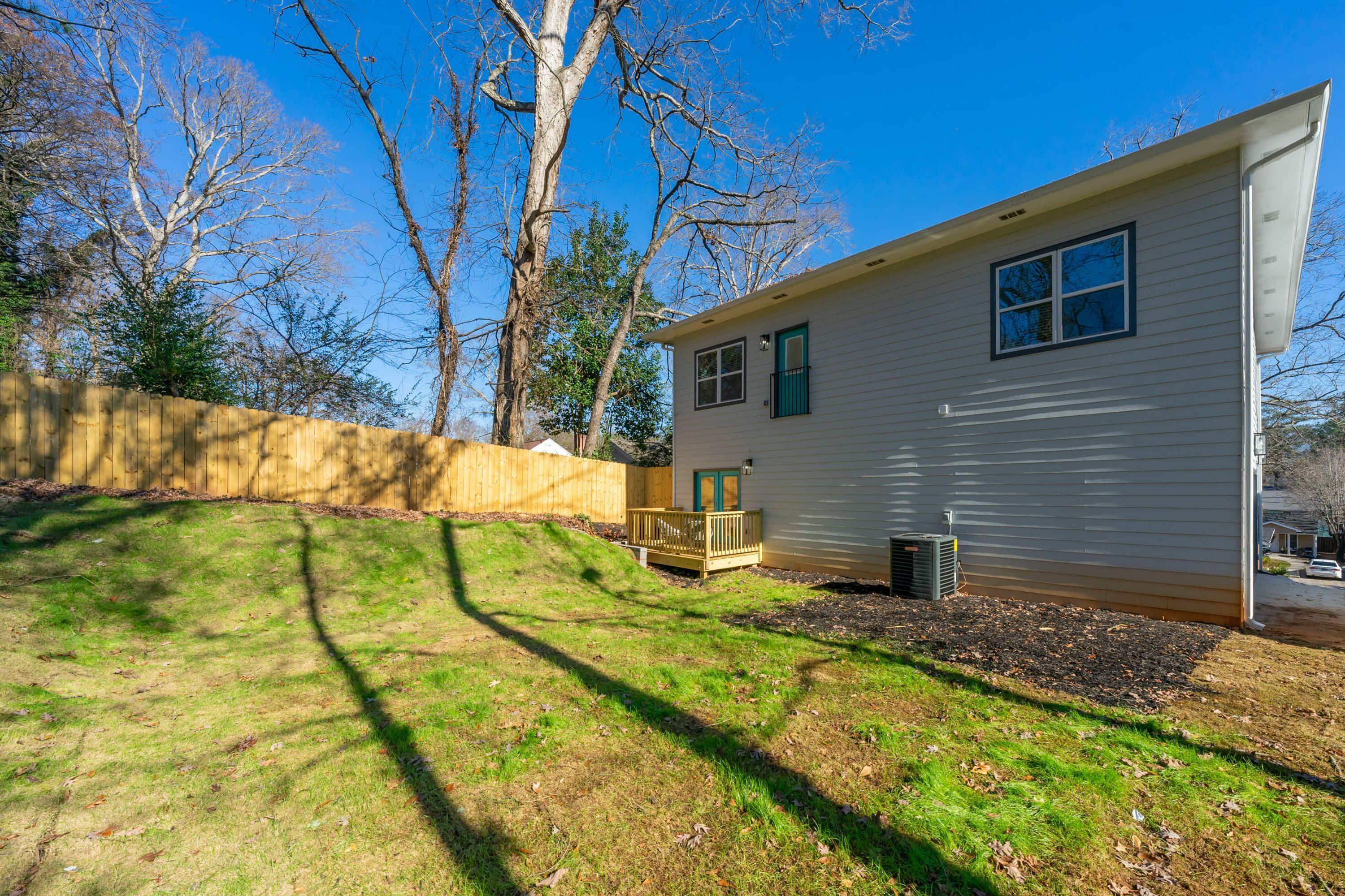 Yhden kerroksen talo, jossa on kuisti, pieni terassi ja piha, joka on aidattu puuaitalla.